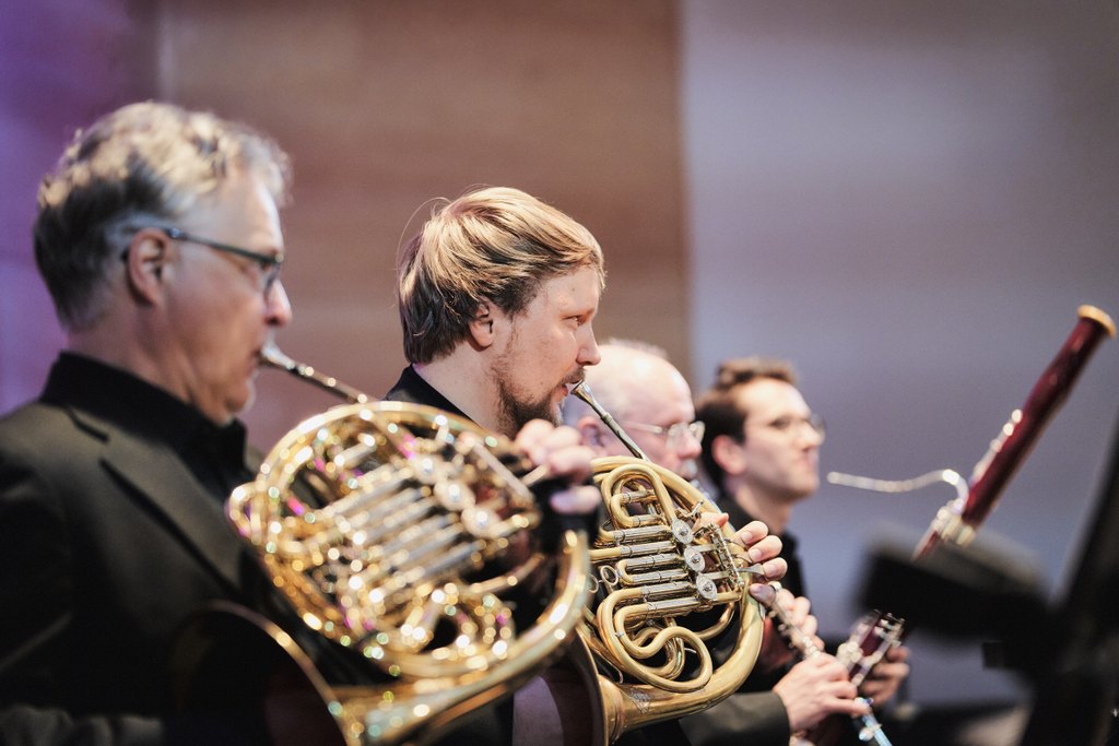 Neljä orkesterimuusikkoa rivissä sivuprofiilista kuvattuna. Kahdella ensimmäisellä on käyrätorvi, kolmannella klarinetti ja neljännellä fagotti.